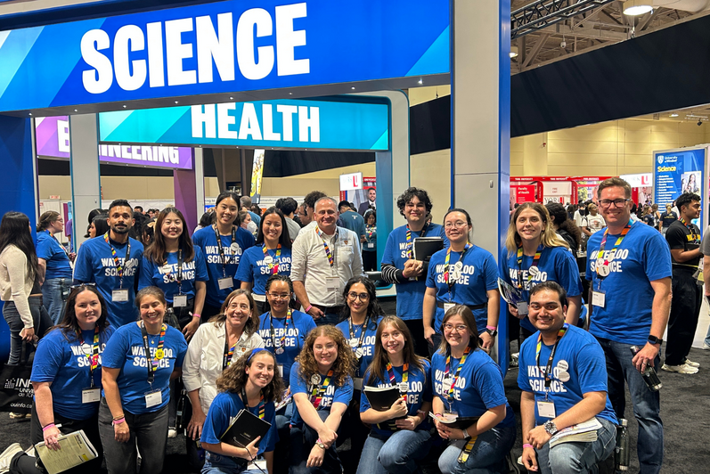 Dean Chris Houser standing in the middle of a group of Science students who are wearing blue t-shirts at the Ontario Universities Fair. 