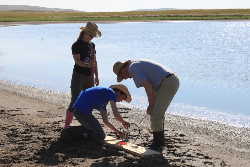 Shaun Frape and two students working on a sandy field site beside a lake