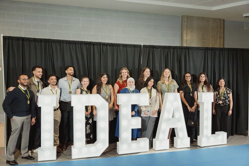 Medal winners standing behind large letters that spell "IDEAL"