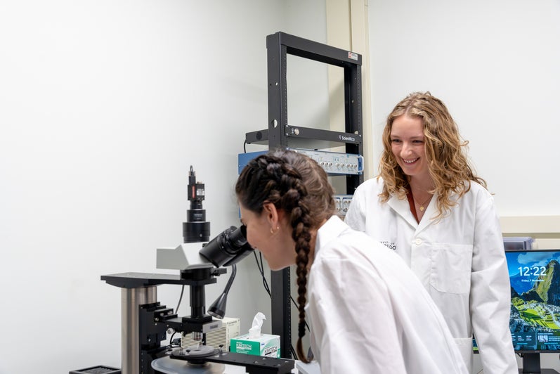 Anne Hambly looking through a microscope with Annemarie Dedek standing next to her