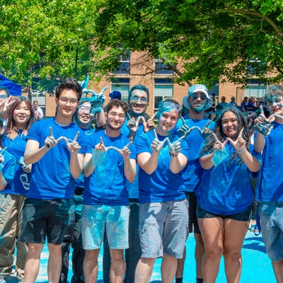 A group of students dyed blue, smiling and holding up a W shape with their fingers