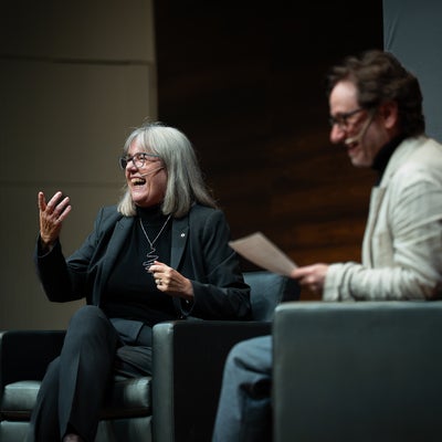 Donna Strickland and Joe Sanderson on chairs on a stage