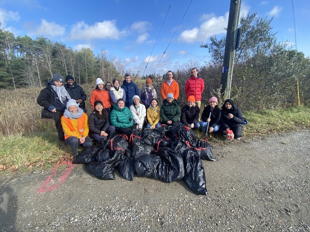 18 volunteers stand behind 20 bags of trash they collected from a wetland.