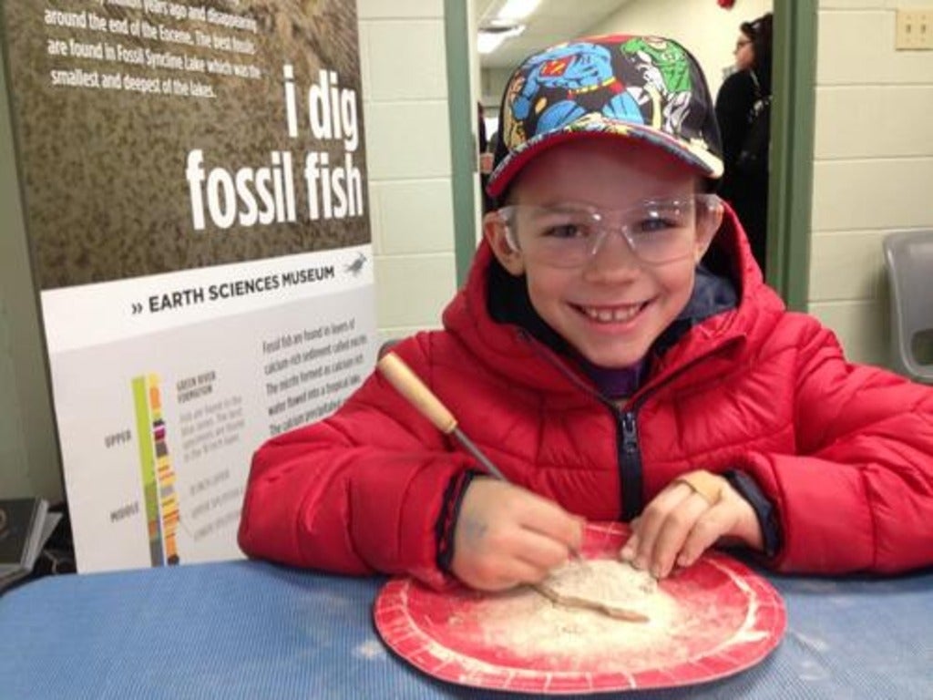boy smiling, etching at a fossil in shale