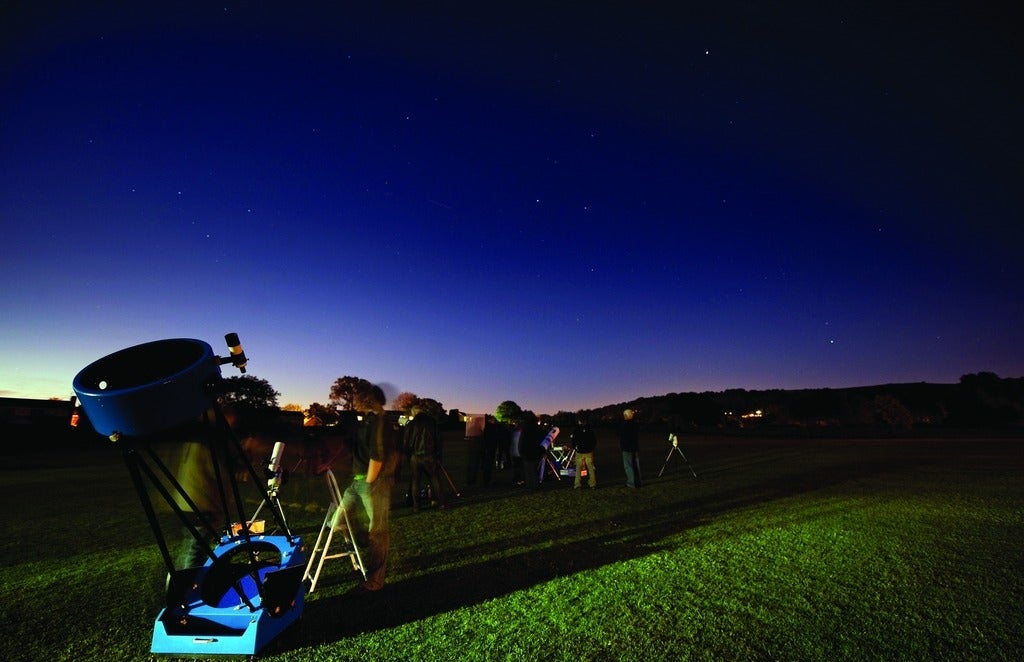 Night sky and telescope on grass.