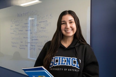 Female student holding books in front of a whiteboard