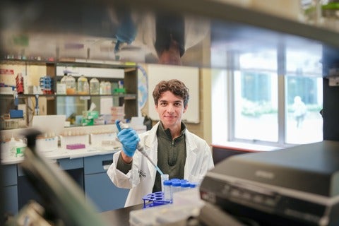 A male student sitting at a lab bench holding a pipette. 
