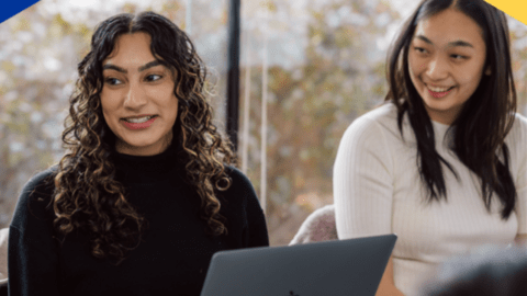 Two students smiling with their laptops open.