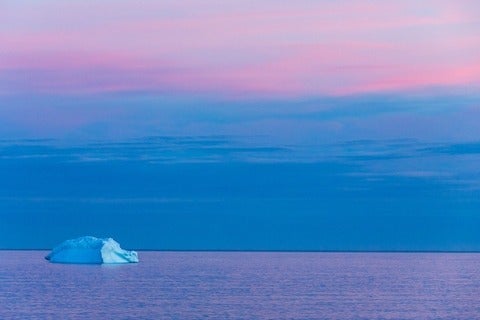Solitary iceberg on the ocean during sunset. The sky and ocean are blue and purple sunset colours