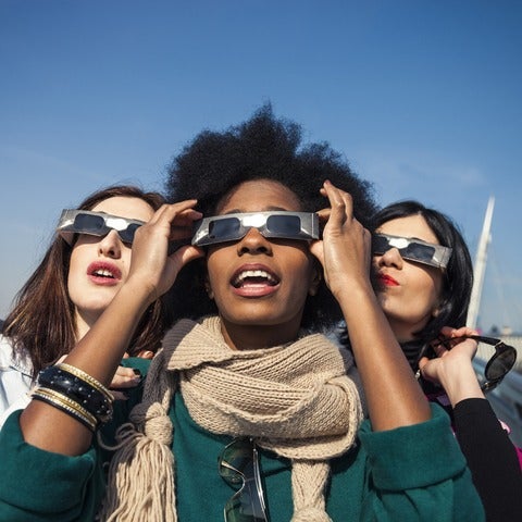 Group of female friends have fun together during a solar eclipse event. Their looking and pointing to the sun wearing the typical glasses normally used to watch a solar eclipse.