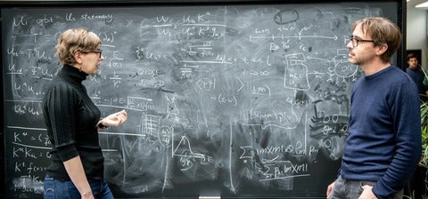 Natalie Paquette and Kevin Costello standing in front of a black board of equations.