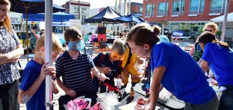 Let's Talk Science volunteer runs a chemistry experiment with 3 children at Kitchener City Hall.