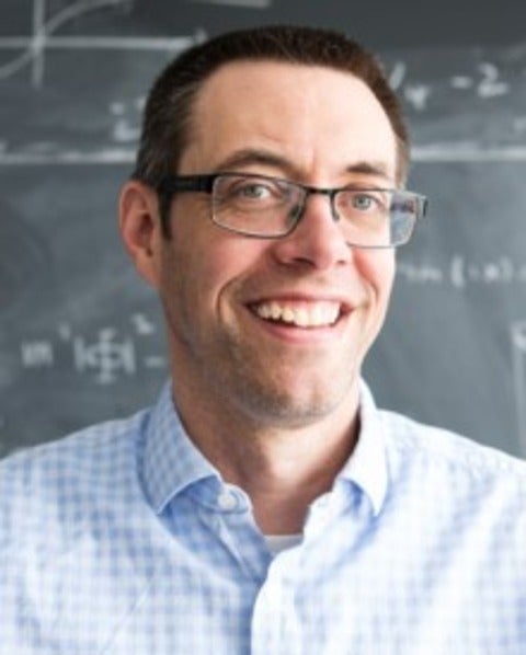 Headshot of Will Percival against a blackboard with equations.