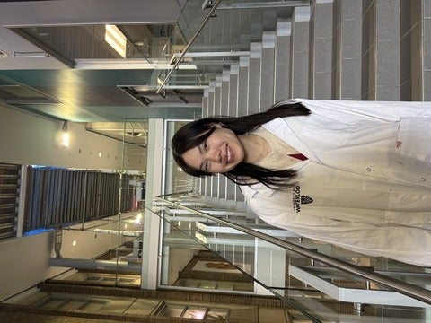 Science Ambassador standing in front of staircase in a white lab coat smiling.