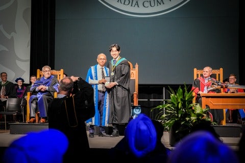 Anthony Dang on stage at convocation accepting the Alumni Gold Medal from University of Waterloo President, Vivek Goel.