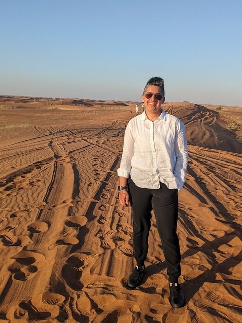 Sophia is standing in the desert in a white shirt and black pants.