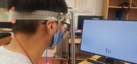 Lab participant wearing head apparatus reading word He on computer screen.