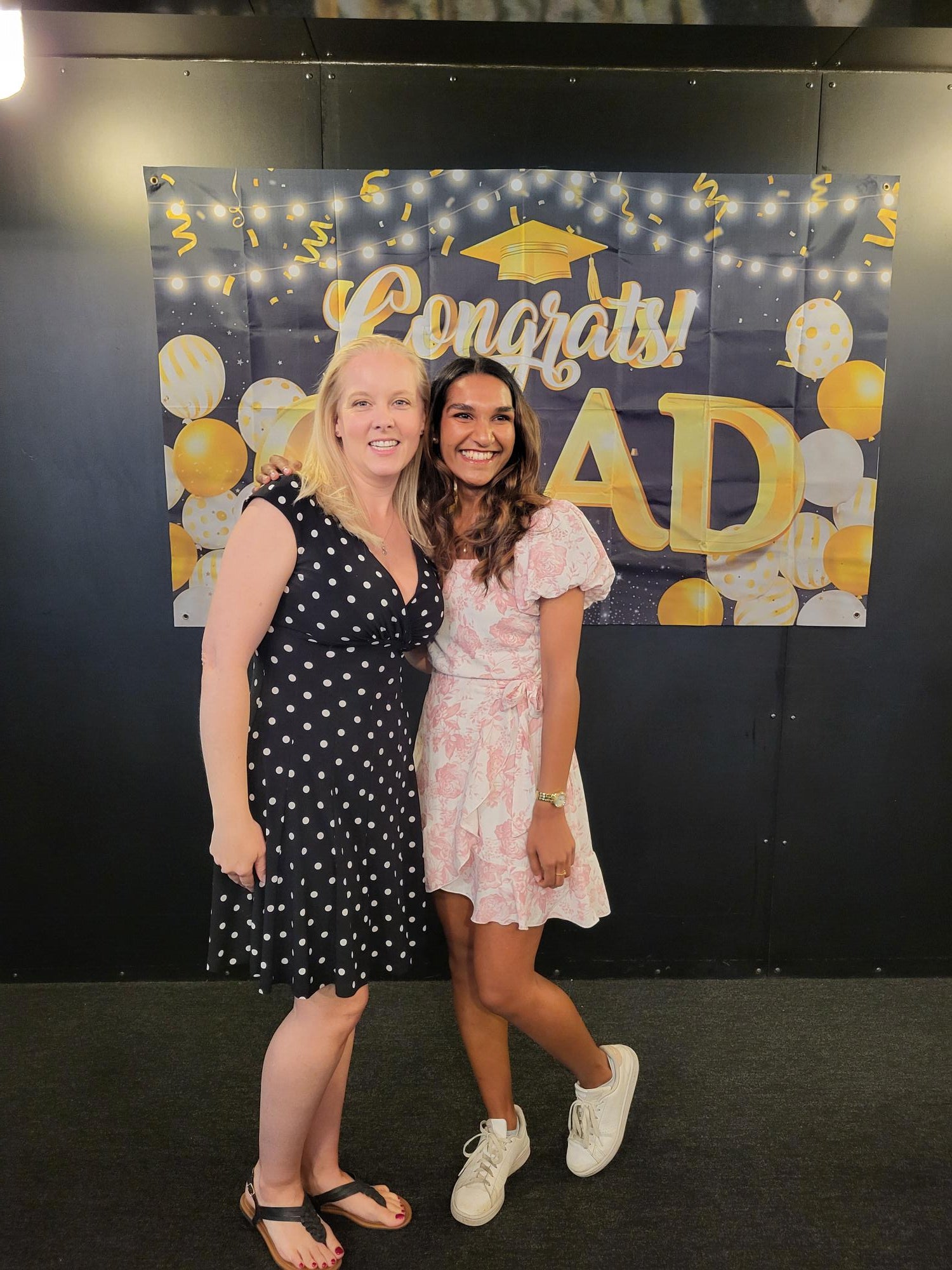 Two undergraduate students posing in front of a sign that says "congrats grad". 
