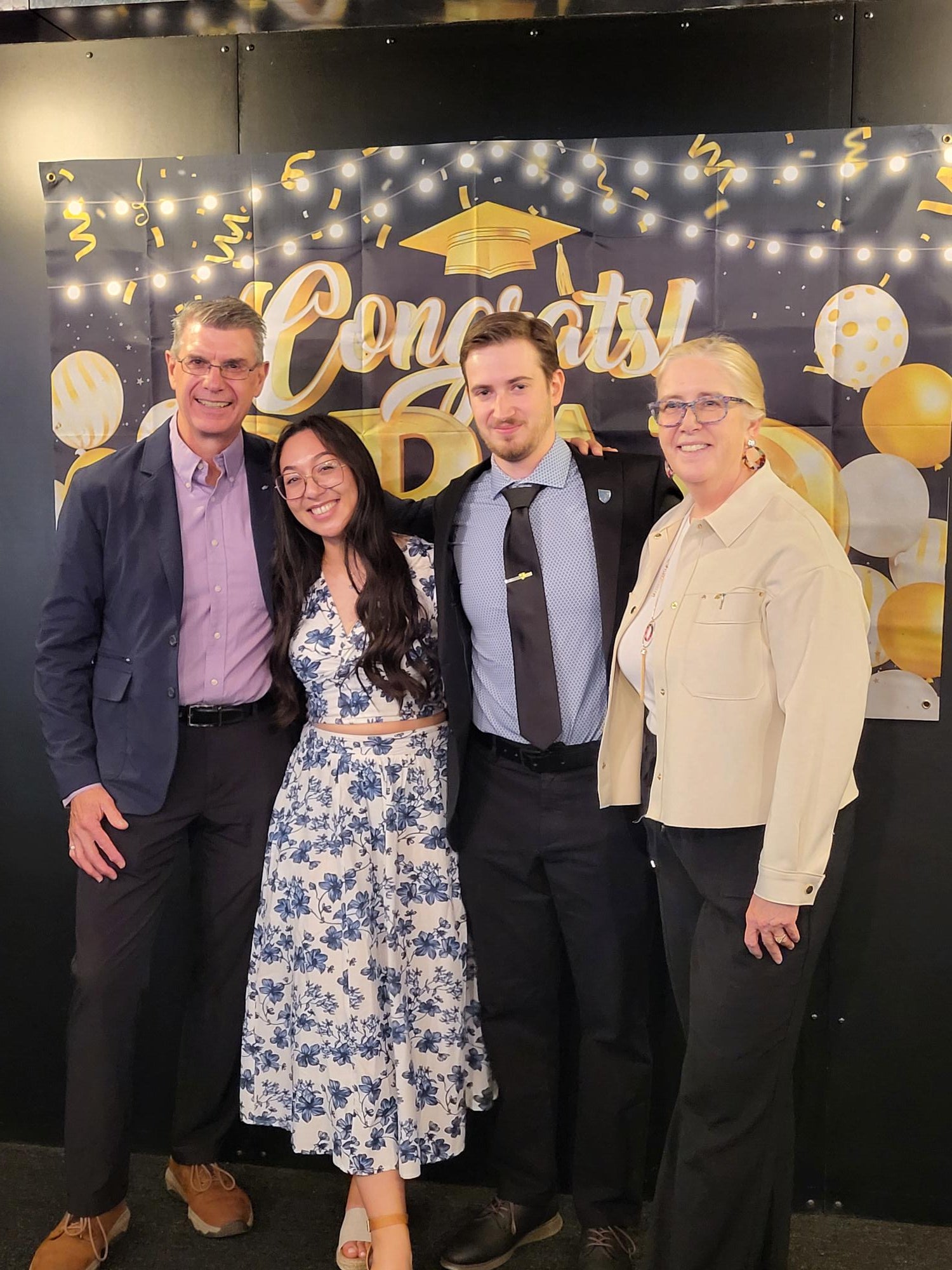 Two undergraduate students posing with professors of Chemistry in front of a graduation sign. 