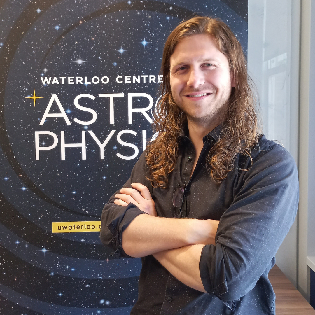 Roan Haggar standing with his arms crossed in front of a banner that says "Waterloo Centre for Astrophysics."