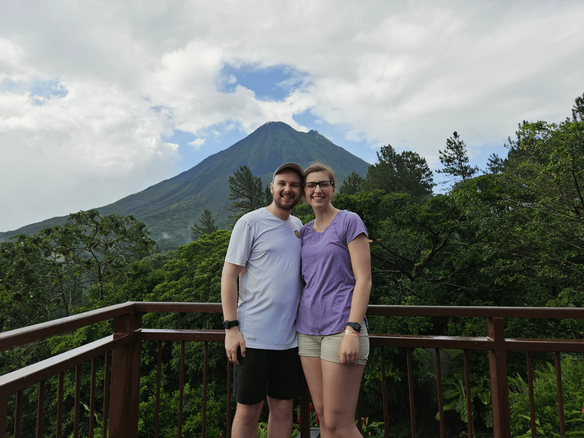 Daniel and Liv standing on a balcony. There is a volcano in the background. 
