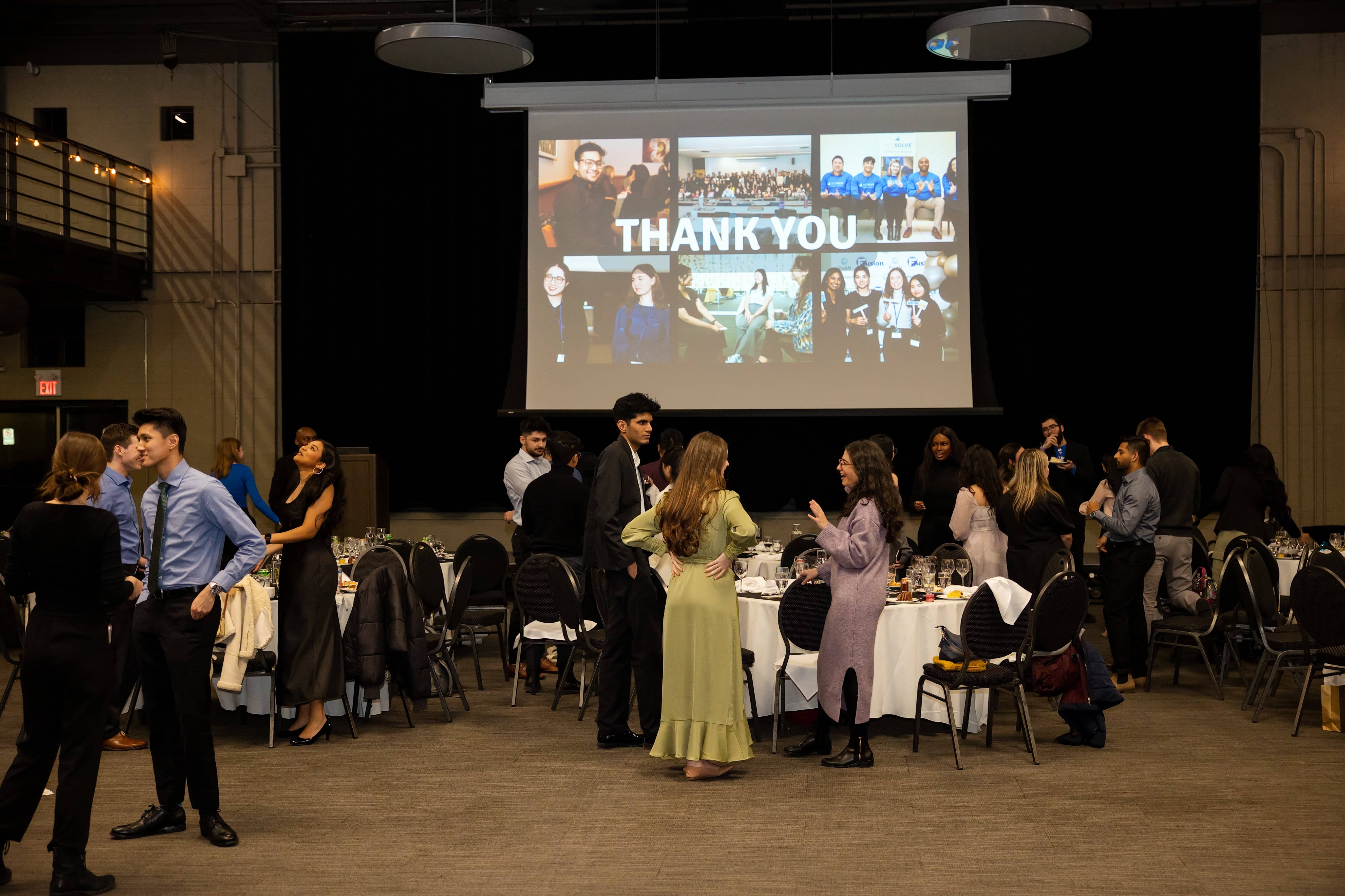 W24 SCBUS showcase: students mingling in front of a slideshow