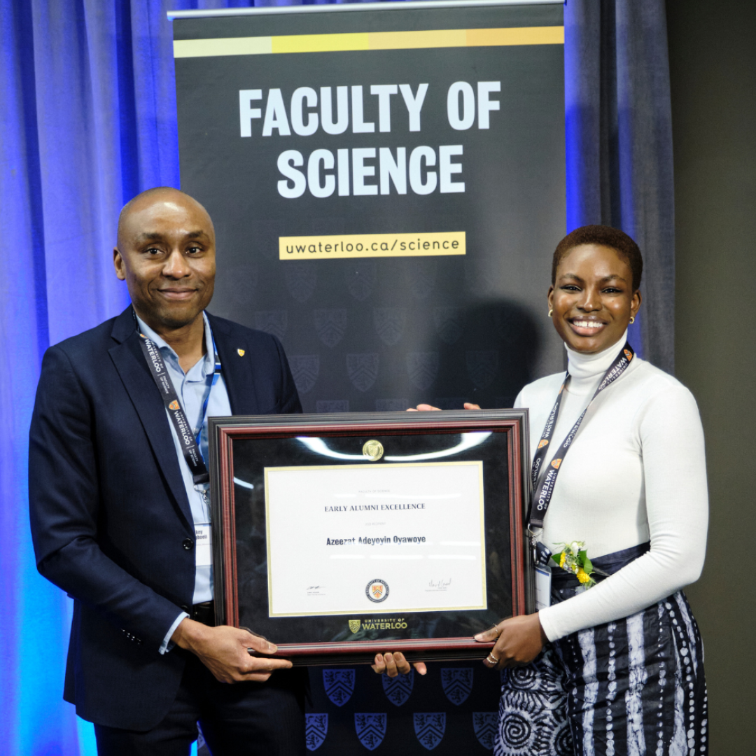 A man and a woman holding a framed award certificate. They are standing in front of a Faculty of Science banner.