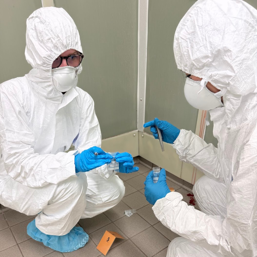 Two students wearing white hazmat suits practicing collecting evidence.