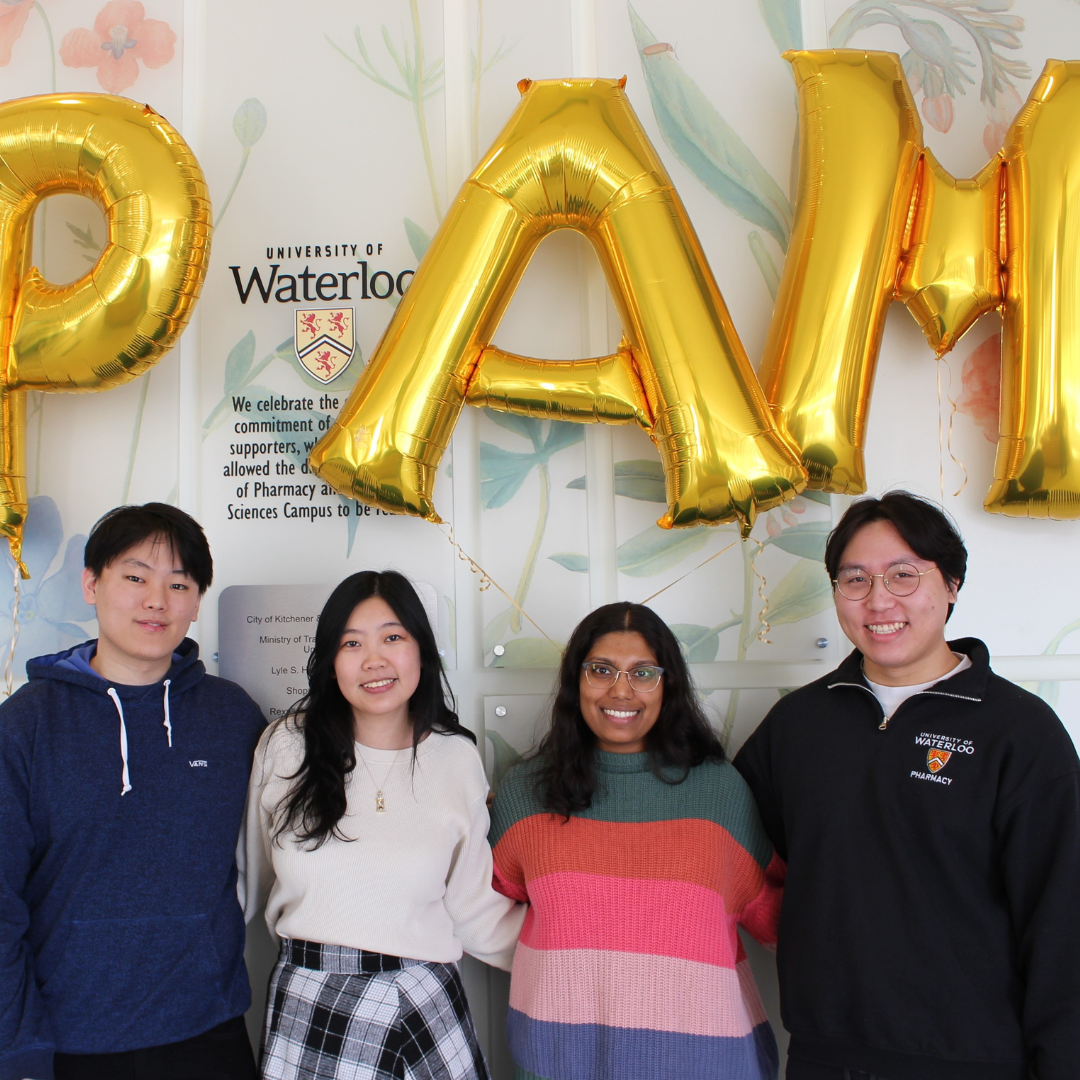 Four pharmacy students standing side-by-side. There are golden balloons that spell "PAM" which stands for Pharmacy Appreciation Month.