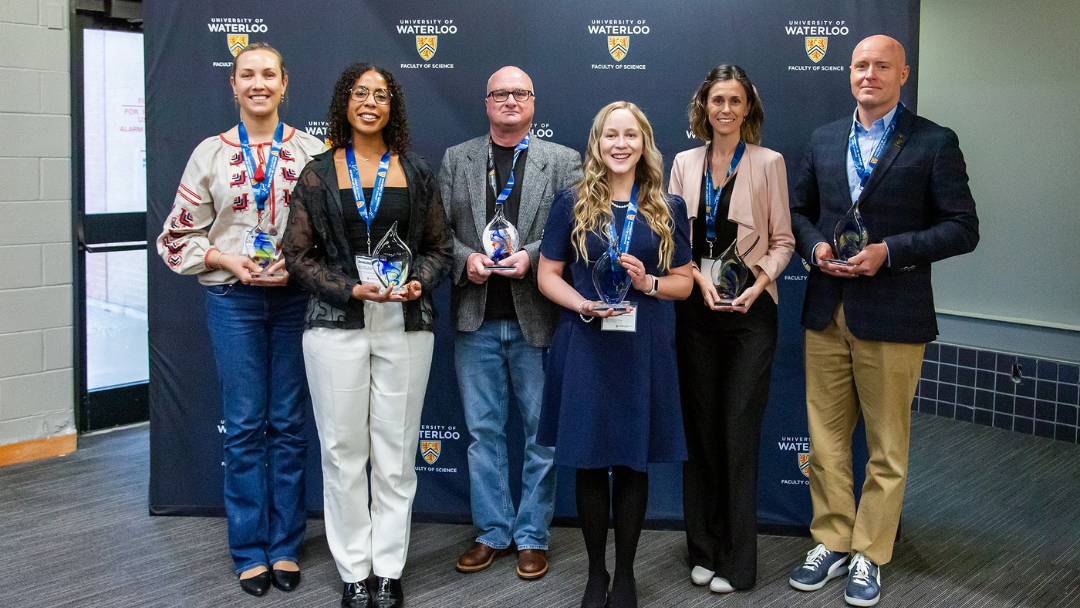 Six science alumni holding their alumni awards. They are standing in front of a University of Waterloo background. 