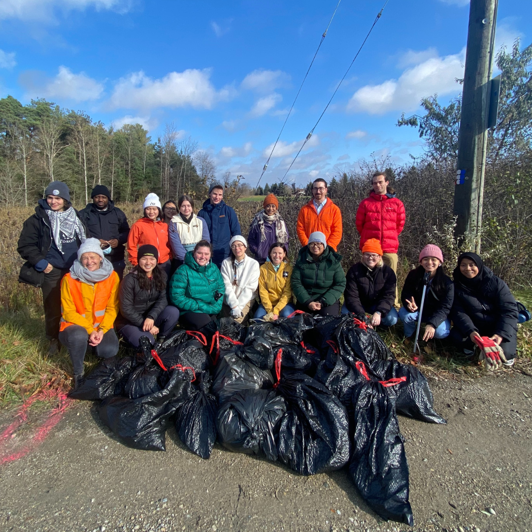 A group of volunteers stand in front of bags full of trash they collected in the wetlands behind them. 