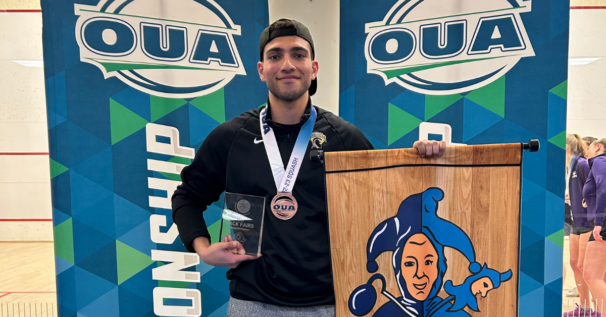 Ahmed holding an OUA medal and a clear glass award plaque in front of blue and green banners reading “OUA” and “Championship.”