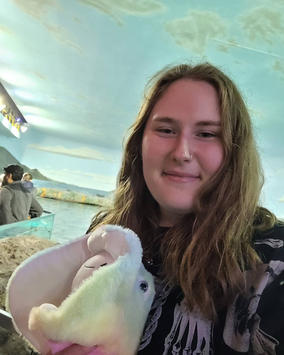 Allison is holding a stuffed animal and is taking a selfie with water in the background. 