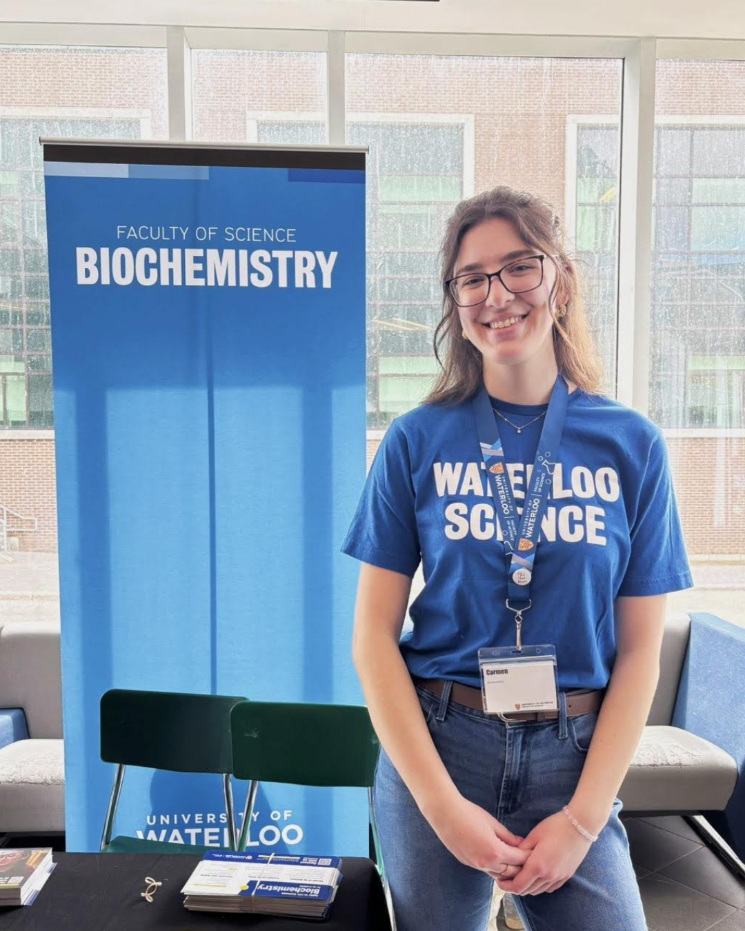 Carmen at an open house even wearing a Science t-shirt standing in front of a pull up banner that says "biochemistry."