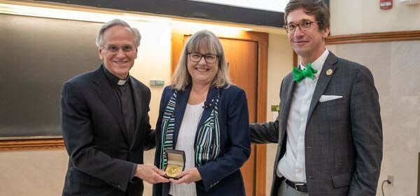 donna holding her medal with a reverend on the right and the dean on the left.