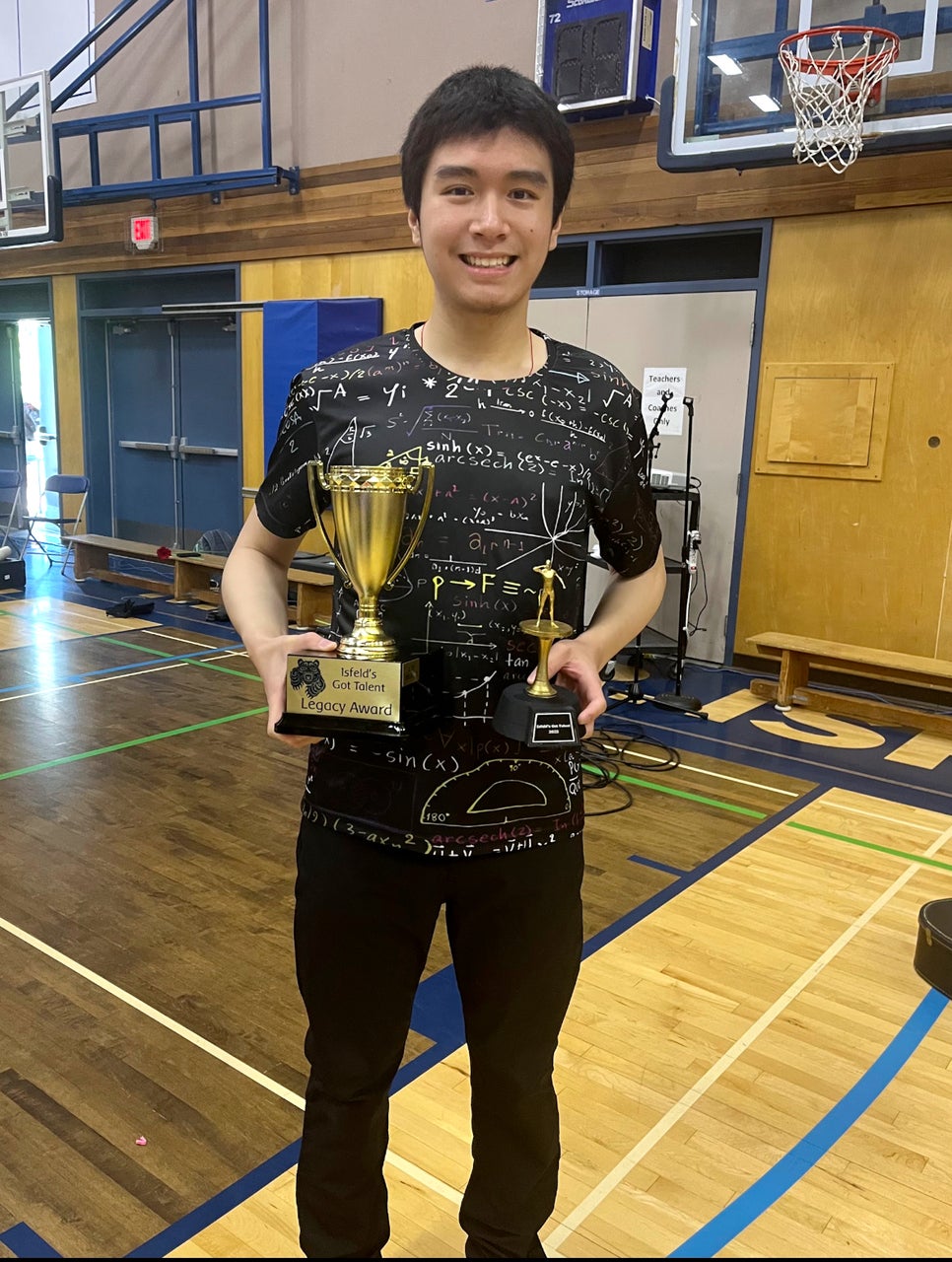 Dio Hsieh standing in a high school gym holding two trophies.