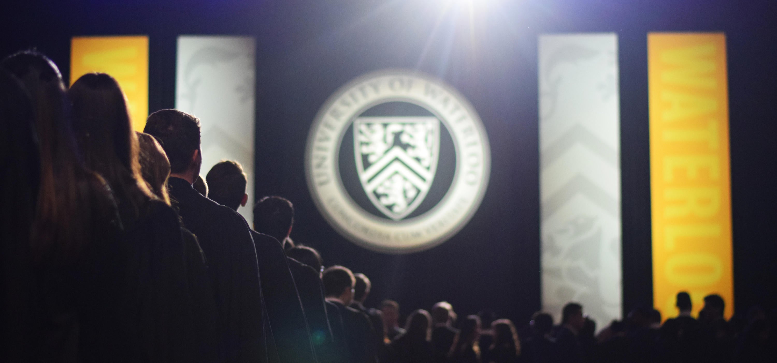Shadow of students in line at convocation with the University of Waterloo emblem in the background