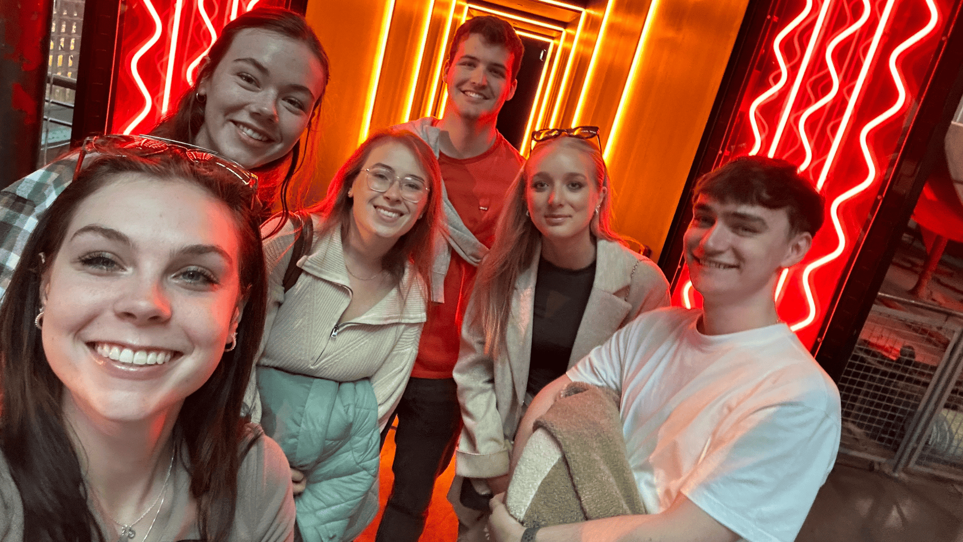 Emma Ross and friends smiling at the camera. There are glowing orange and red lights behind them.