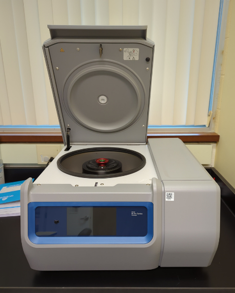 A rectangular benchtop instrument approximately the depth of a lab bench, and the width of a drawer. The top is open by a hinge at the back of the instrument, and shows a circular cavity inside.
