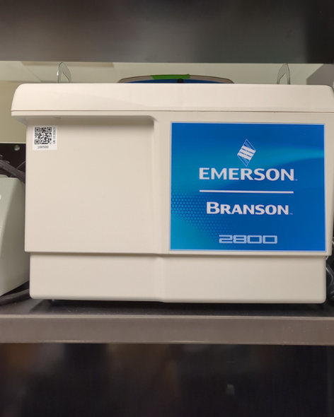 A small rectangular instrument sitting on a shelf, with a sticker reading Emerson | Branson | 2800.