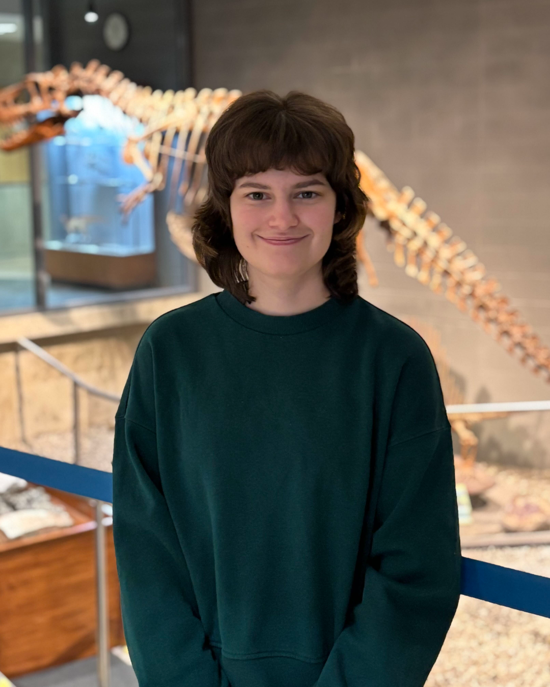 Grace wearing a green sweatshirt standing inside the dino pit at the Earth Sciences museum.