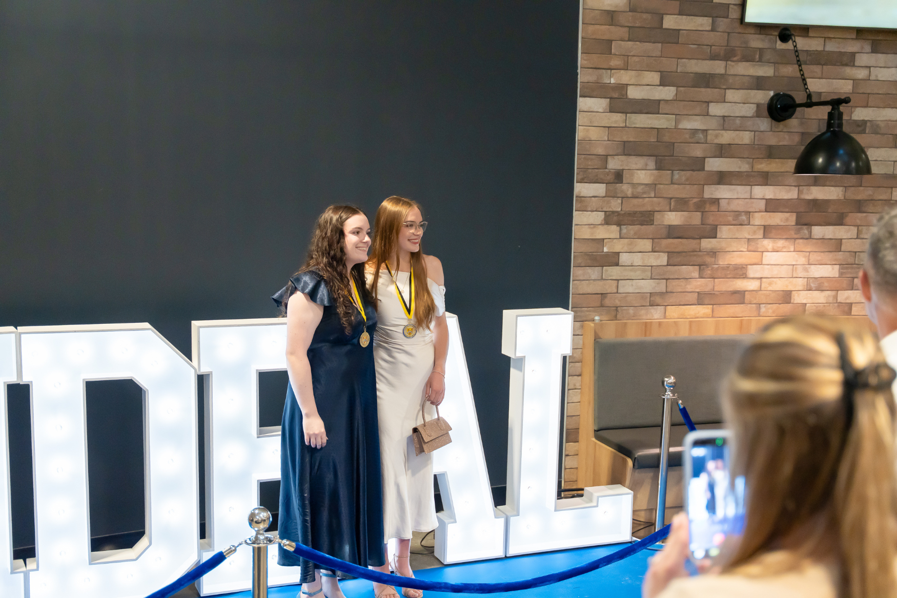 Two students posing in front of a light up IDEAL sign.