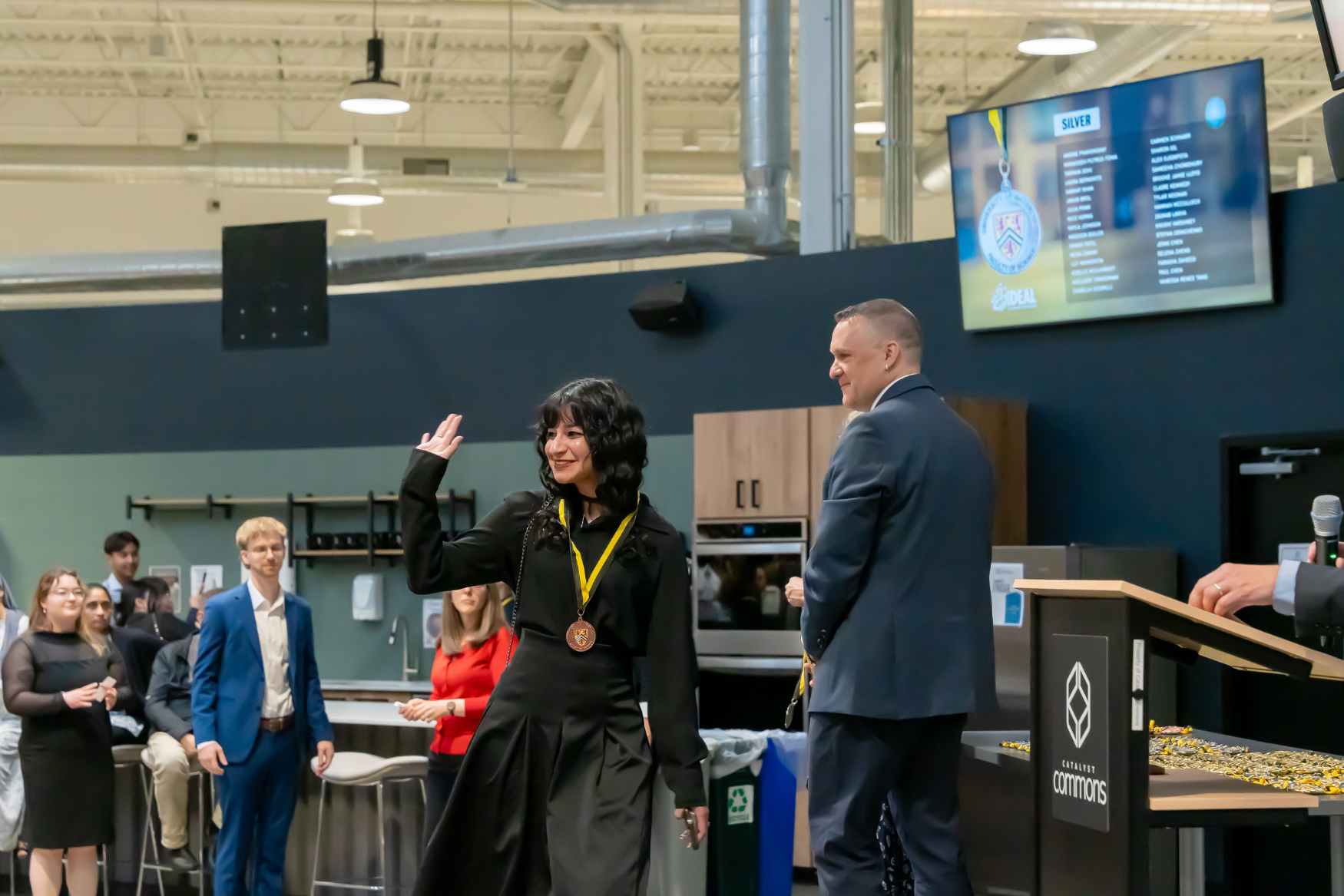 A student walking across the stage and waving at the IDEAL Scholar ceremony.
