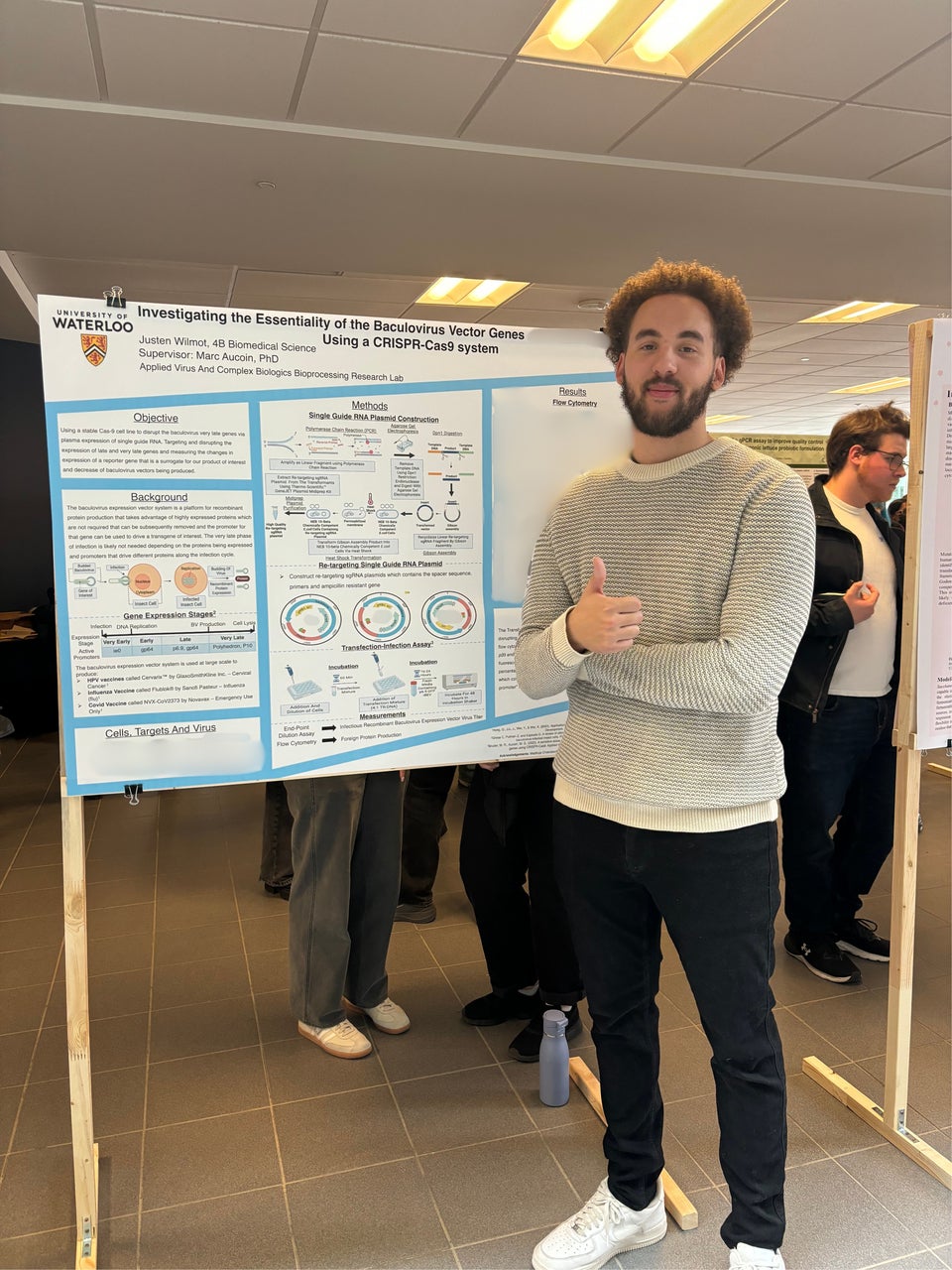 Justen is giving the thumbs up. He is standing in front of a poster presentation of his research.