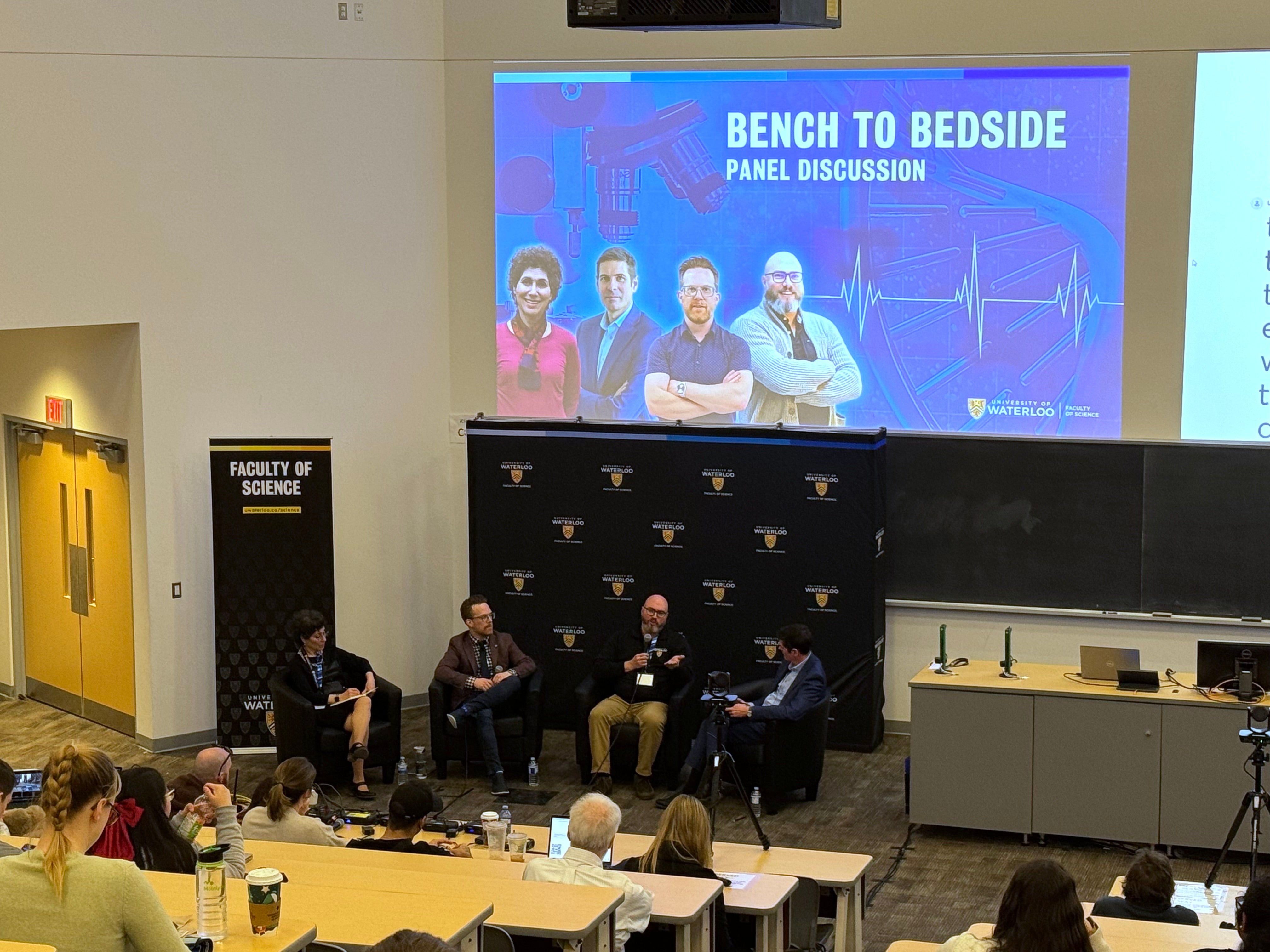 A panel discussion at the front of the room with an attentive audience looking on