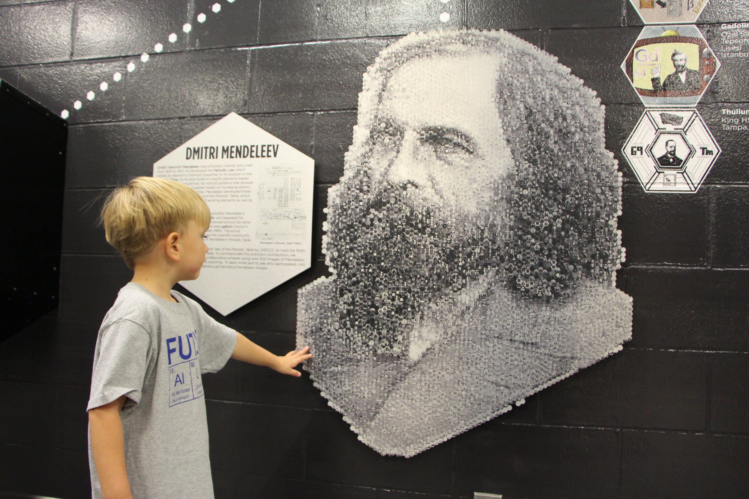 Child standing and looking at a mosaic of Dmitri Mendeleev.