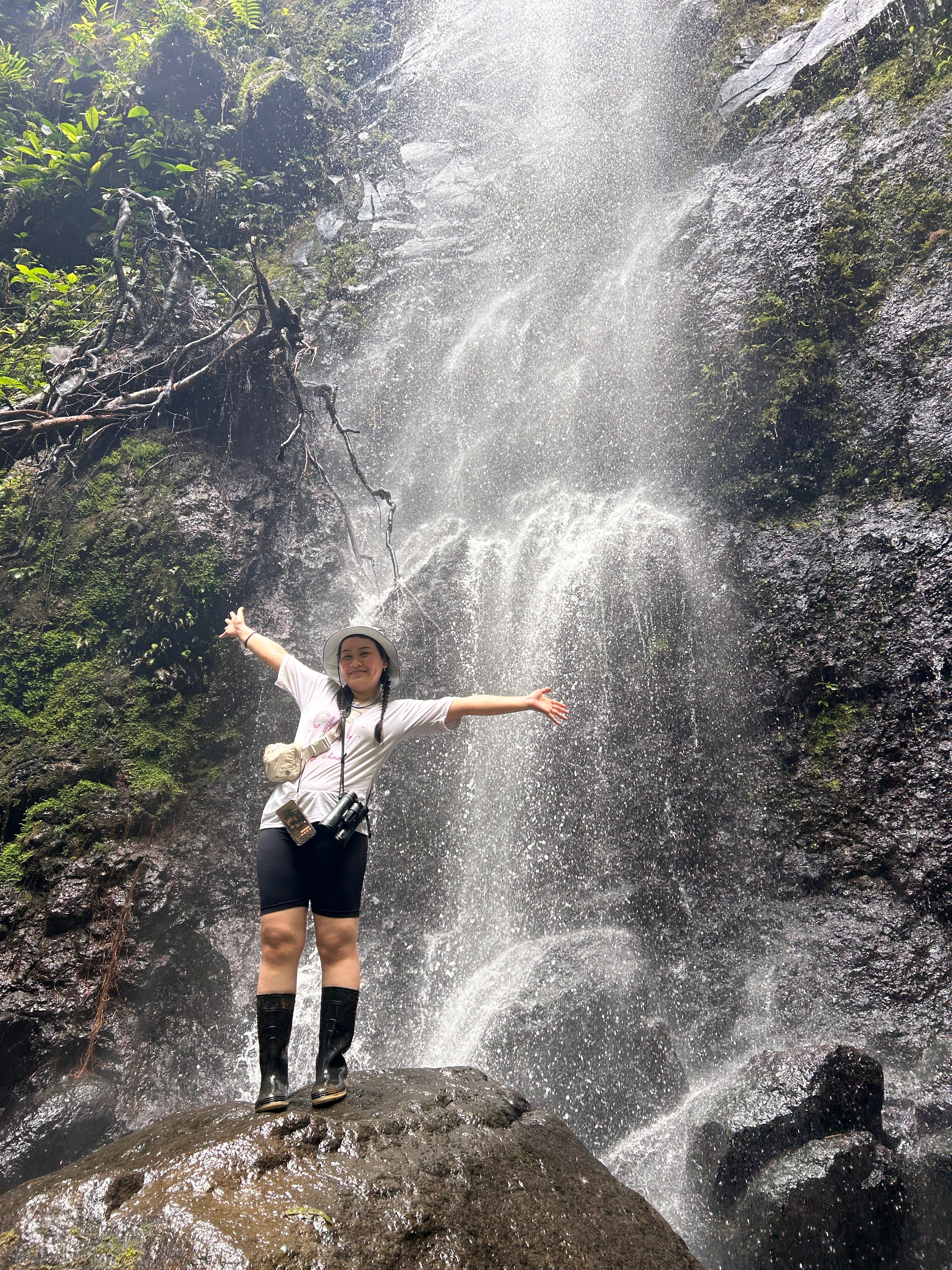 An alumni posing on a rock in front of a waterfall