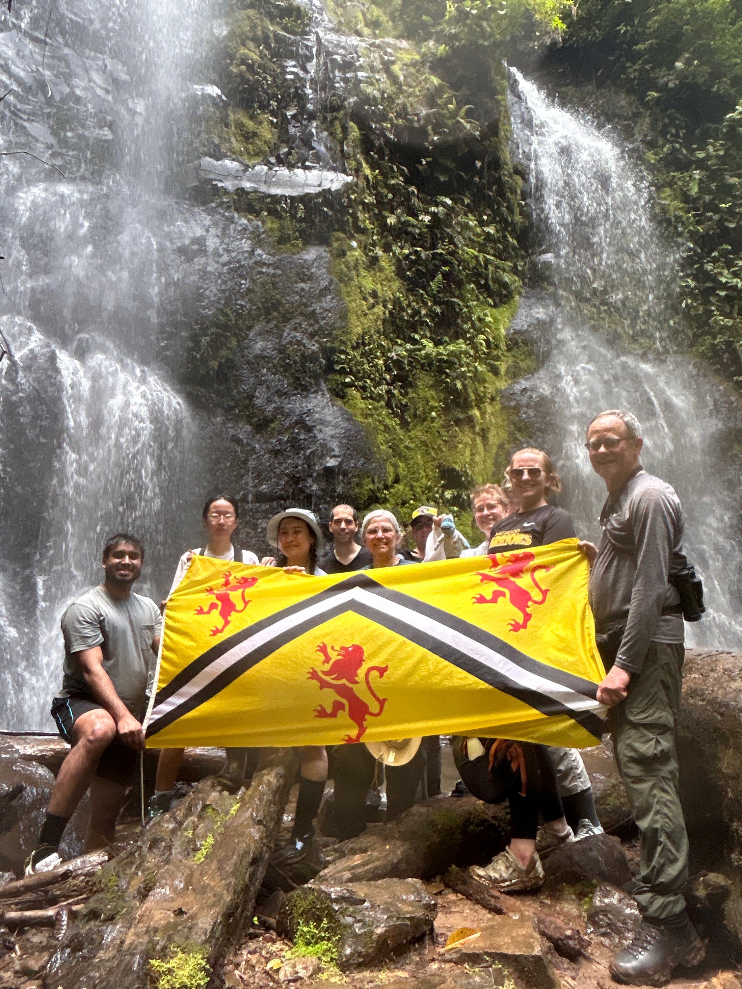 Group of alumni at the base of a waterfall, holding the UWaterloo flag