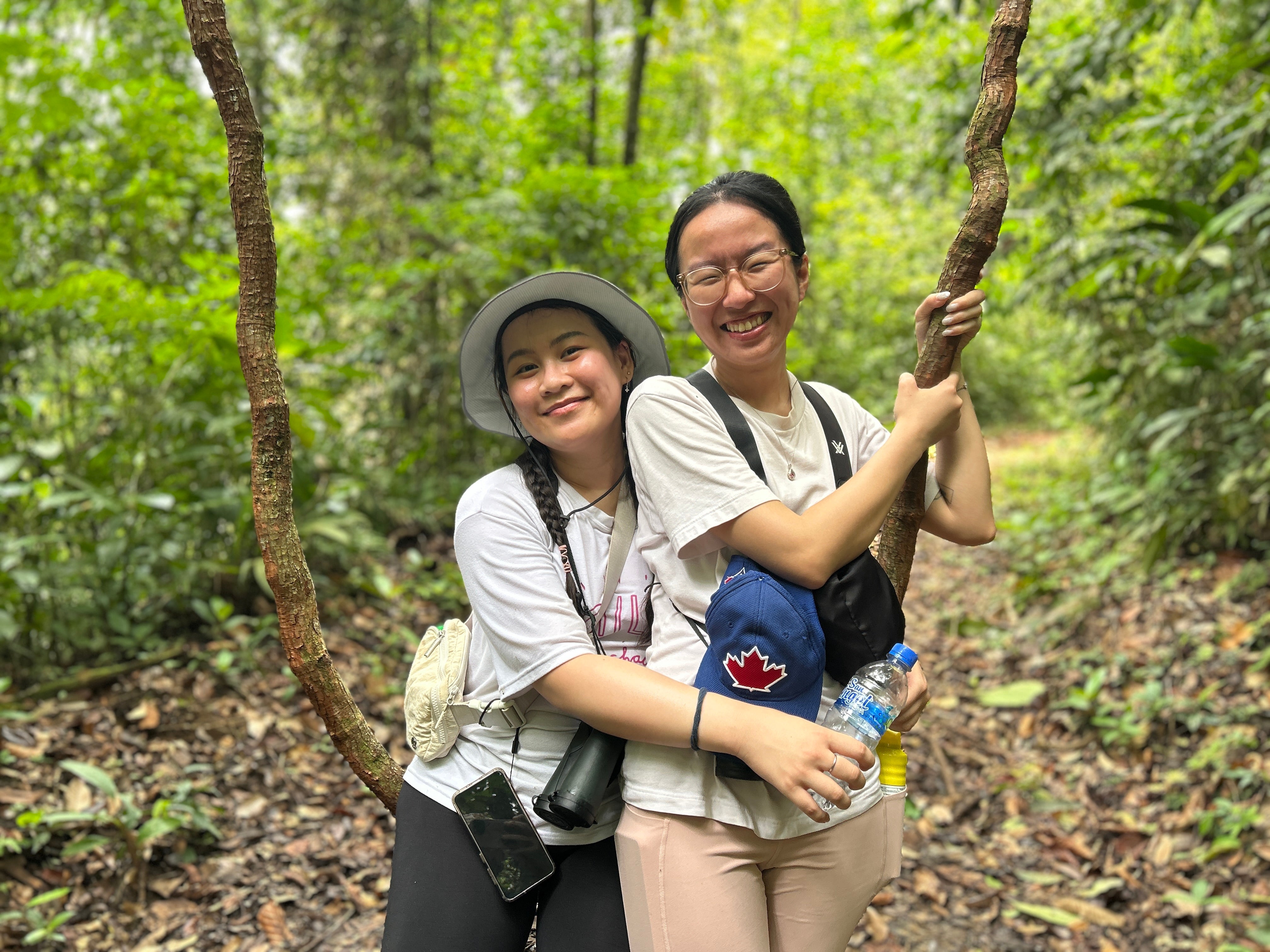 Two young alumni hugging on a path in the rainforest