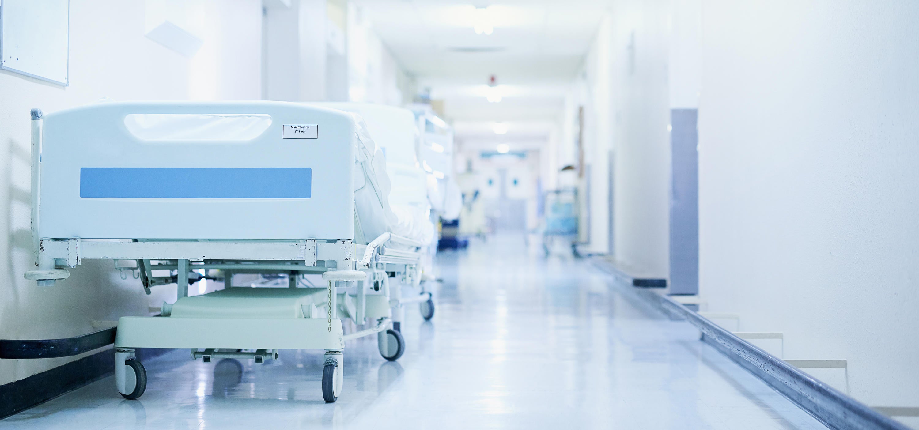 Stock photo of a hospital hallway with an empty bed on the left side.